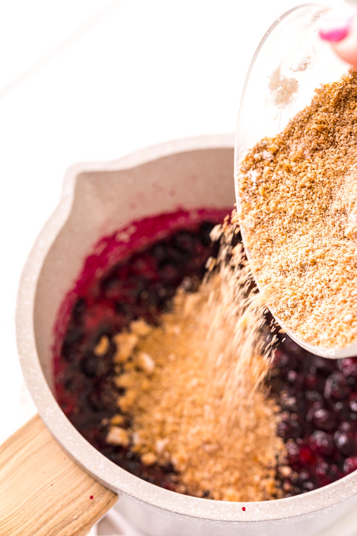 spices being added to a pot of simmering blueberries.