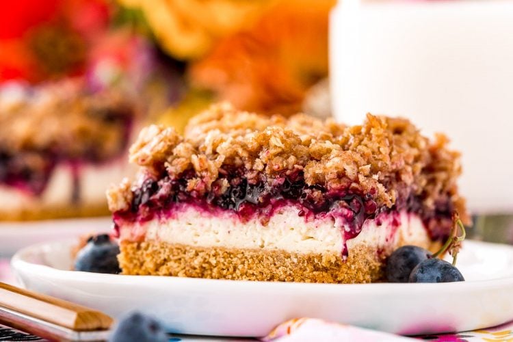 Slice of blueberry cheesecake with crumble topping on a white plate.