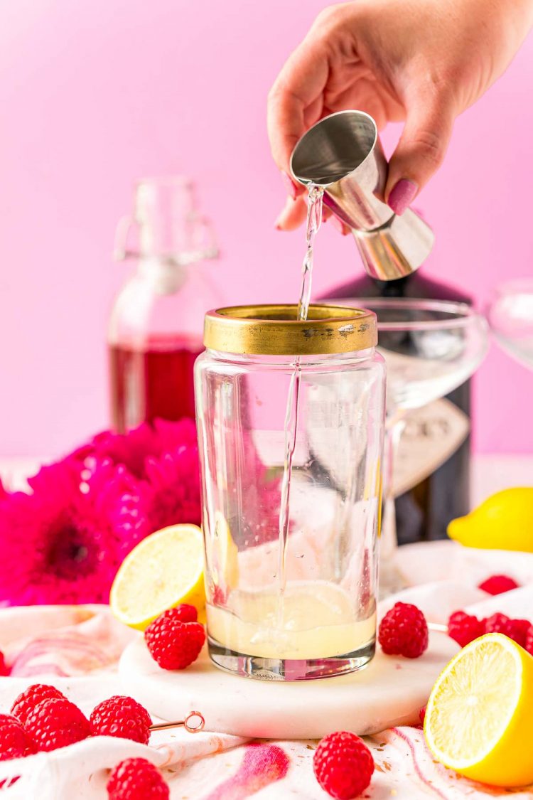 Gin being poured into a cocktail shaker with lemon juice.