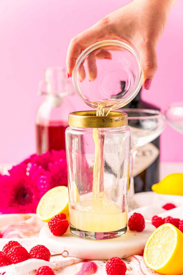 Egg white being added to a cocktail shaker with gin and lemon juice.