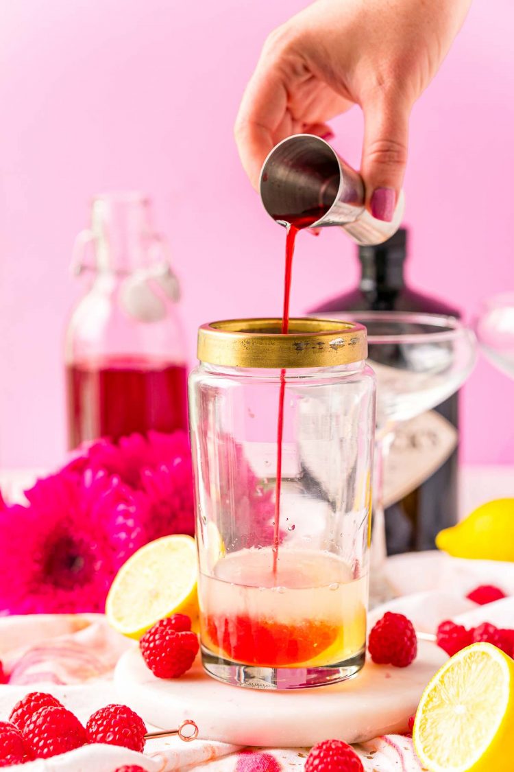 Raspberry simple syrup being added to a cocktail shaker with egg white, gin, and lemon juice.