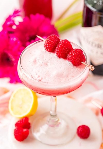 A cocktail glass filled with a pink foamy cocktail garnished with raspberries.