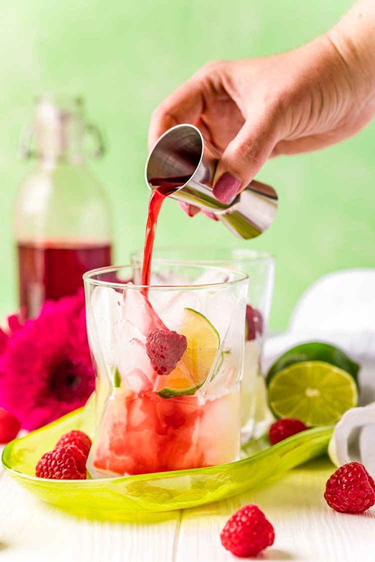 Raspberry simple syrup being poured into a glass with ice and lime juice in it.