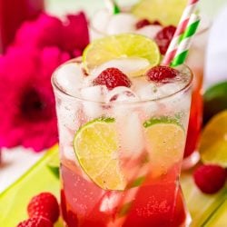 A glass filled with a raspberry lime rickey on a green serving tray with raspberries around it.