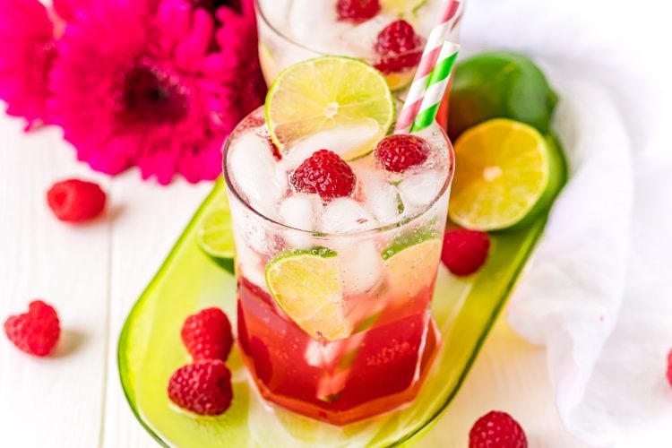 Two raspberry lime rickeys on a green serving tray with raspberries around it. 