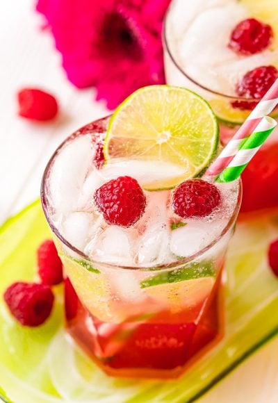 A glass filled with a raspberry lime rickey on a green serving tray with raspberries around it.