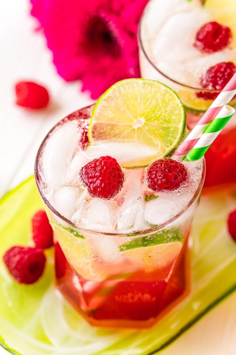 A glass filled with a raspberry lime rickey on a green serving tray with raspberries around it.