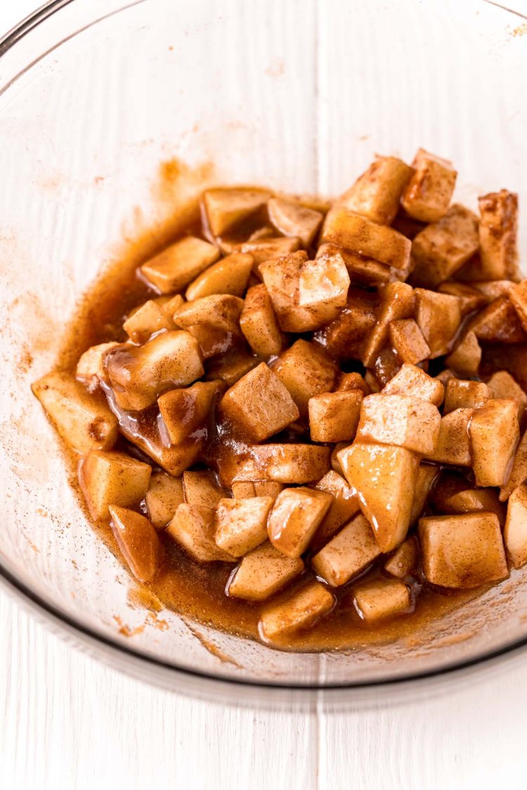 Apples tossed with brown sugar, cinnamon, and lemon juice in a glass mixing bowl.