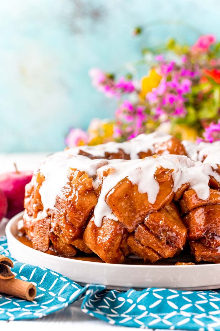 Apple cinnamon roll monkey bread on a white plate on a blue napkin covered in icing.