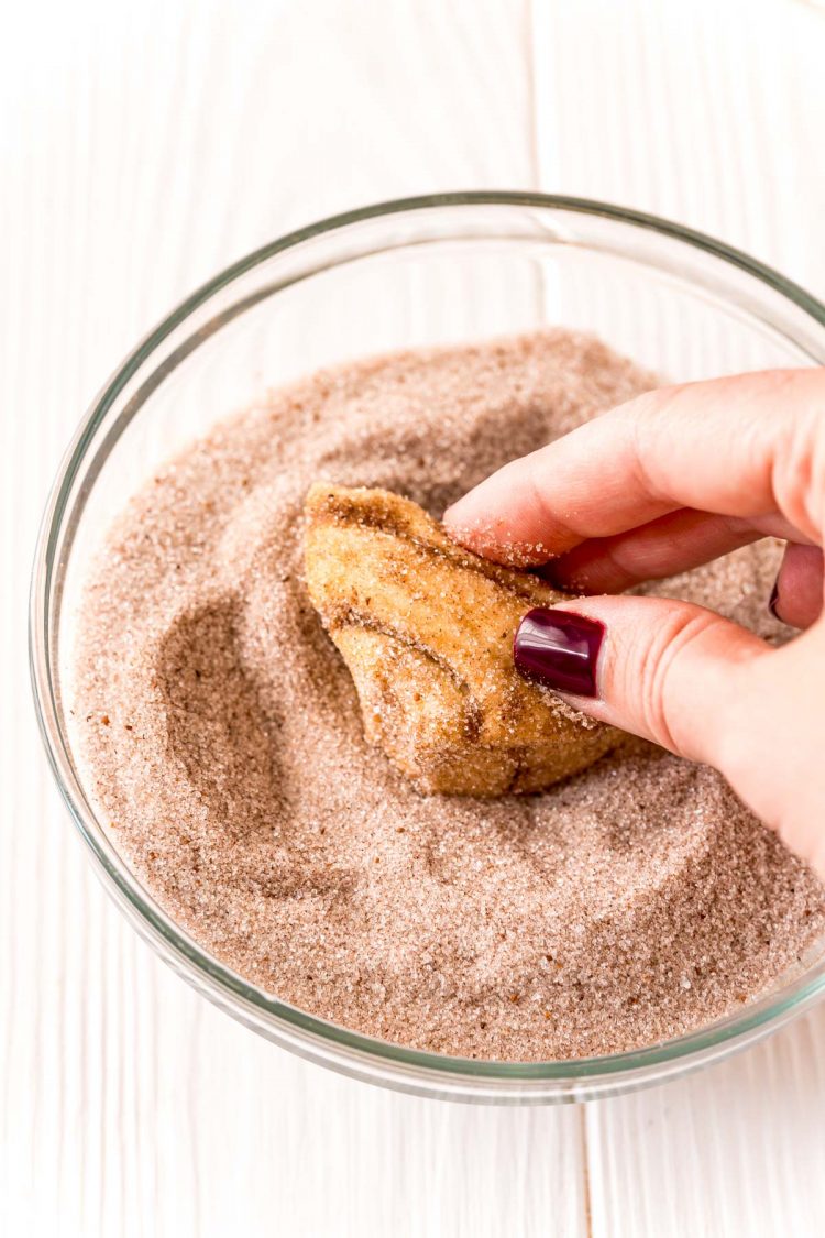 A piece of cinnamon roll dough being rolled in cinnamon sugar.