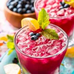 Close up photo of a glass filled with a blueberry cocktail.