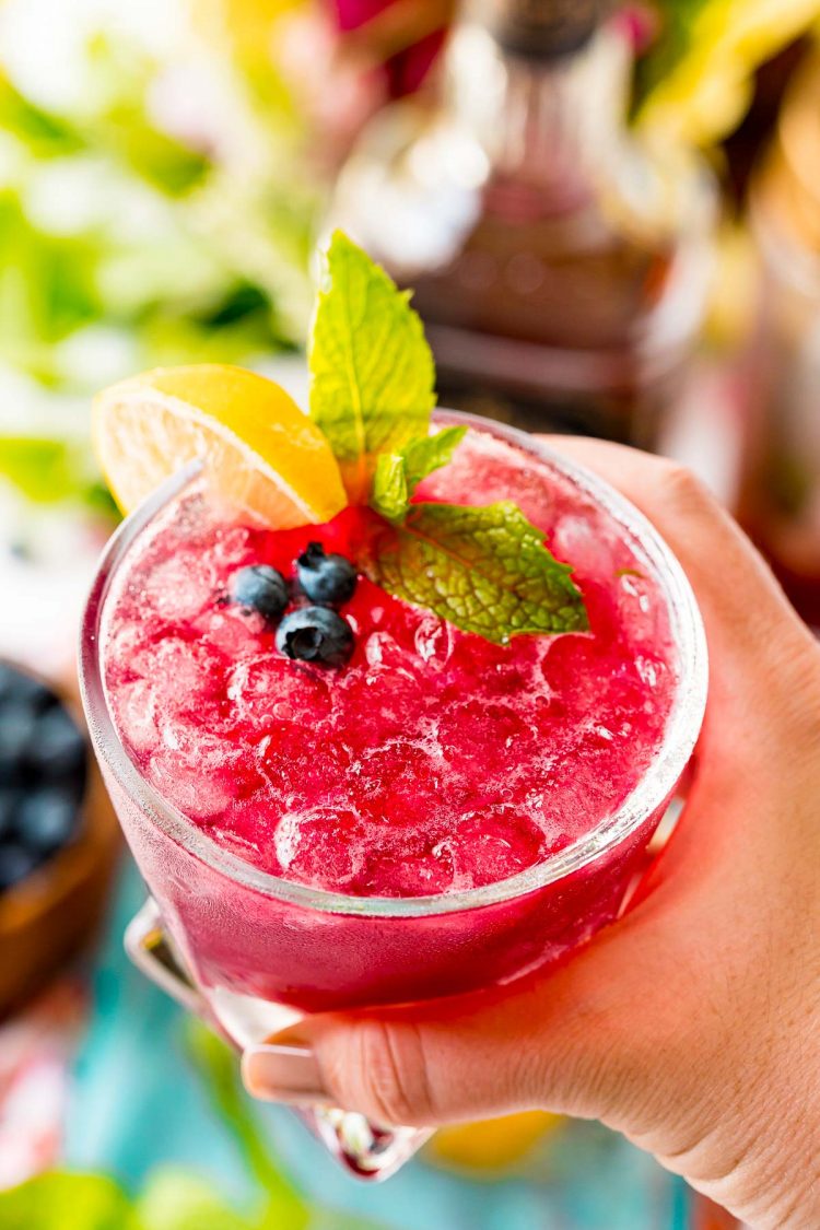 Woman's hand holding a blueberry cocktail up to the camera.