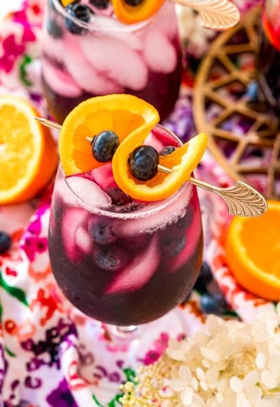 Close up photo of a glass of blueberry sangria topped with a orange slice and blueberries.
