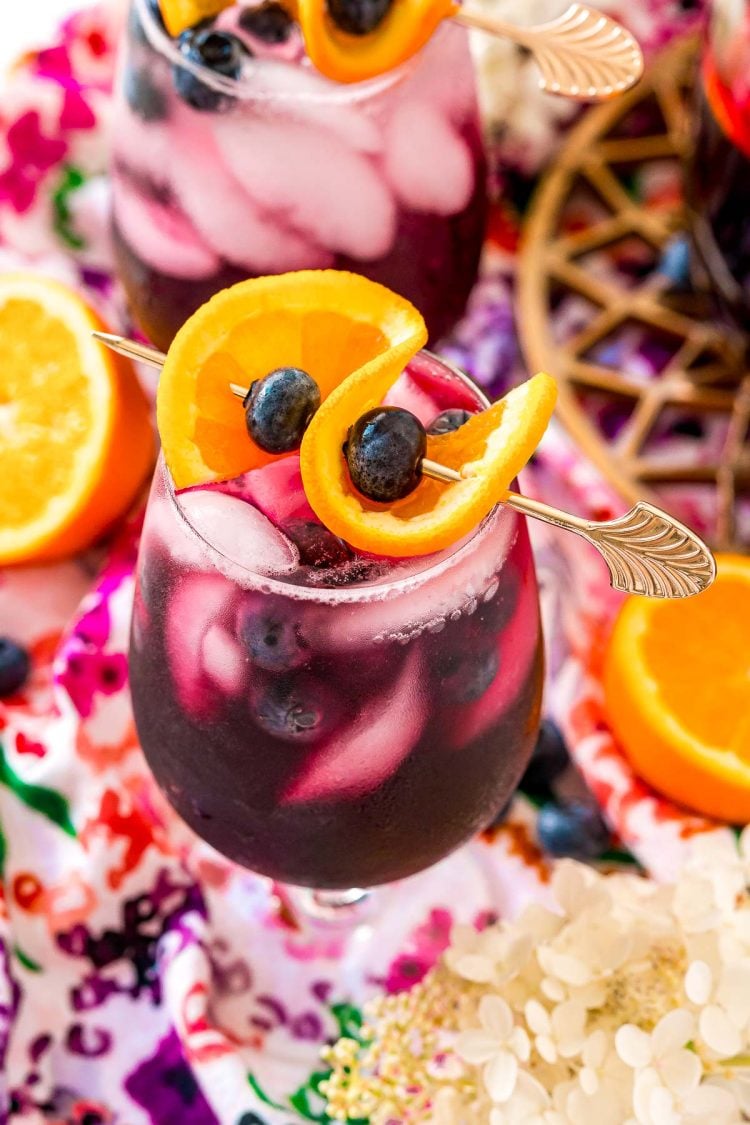 Close up photo of a glass of blueberry sangria topped with a orange slice and blueberries.