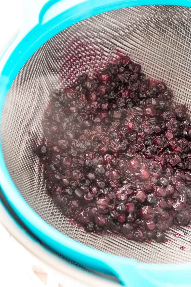 Blueberries being strained through a fine mesh strainer.