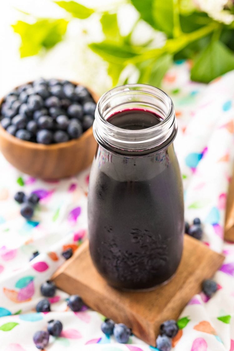 Blueberry simple syrup in a small bottle with blueberries in the background.