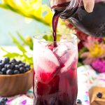 Blueberry simple syrup being poured into a glass of limeade.