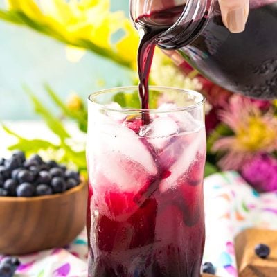 Blueberry simple syrup being poured into a glass of limeade.