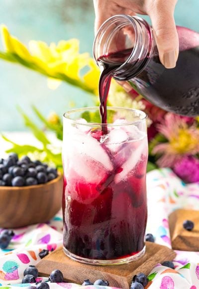 Blueberry simple syrup being poured into a glass of limeade.