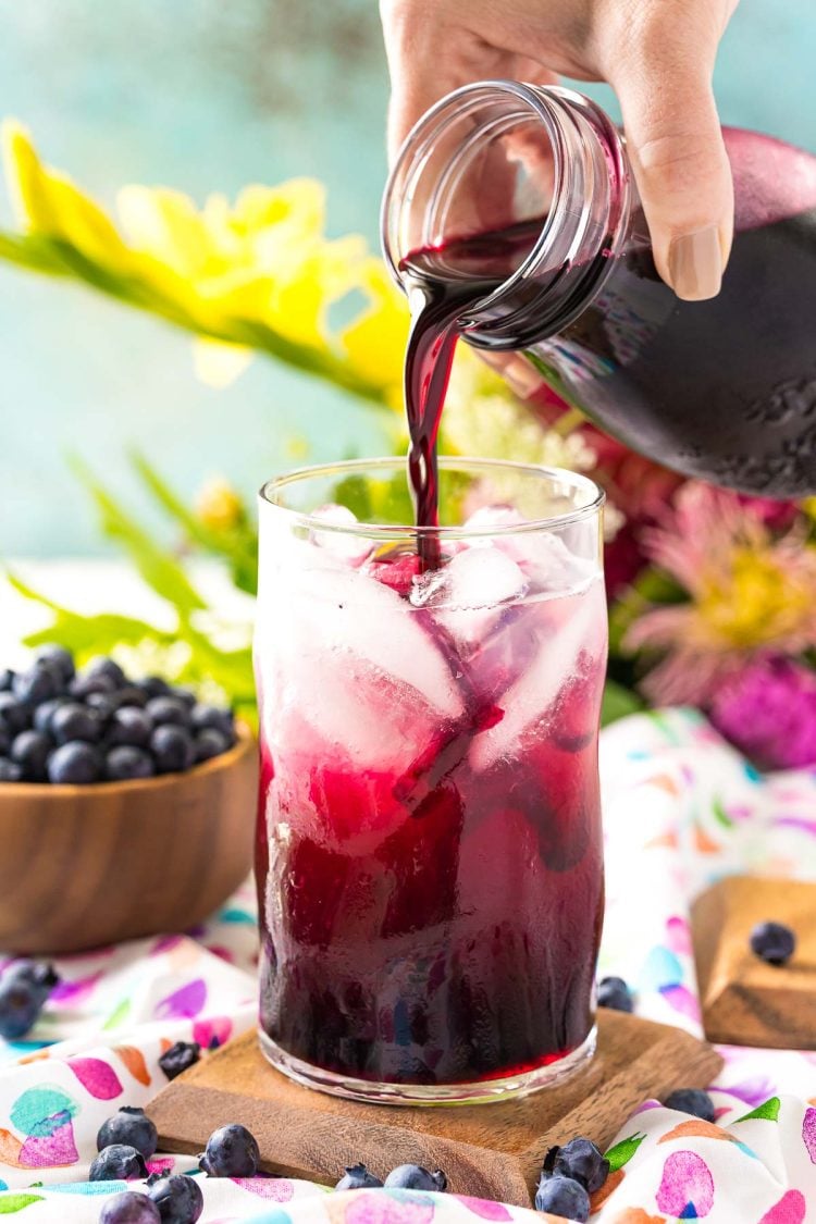 Blueberry simple syrup being poured into a glass of limeade.