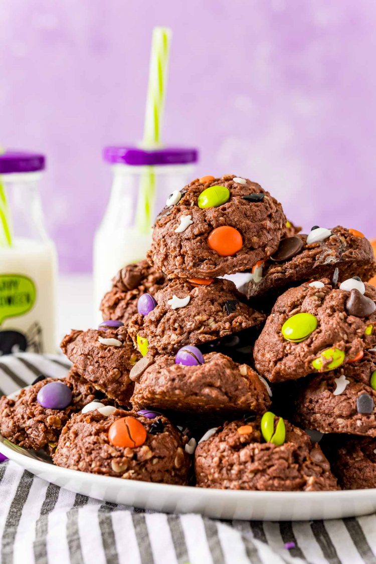 Halloween chocolate cookies on a white plate with a purple background and glasses on milk in the background.