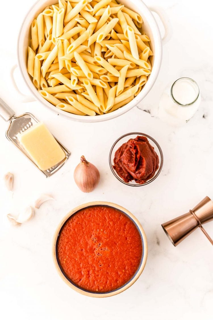 Ingredients to make vodka sauce on a white marble table.