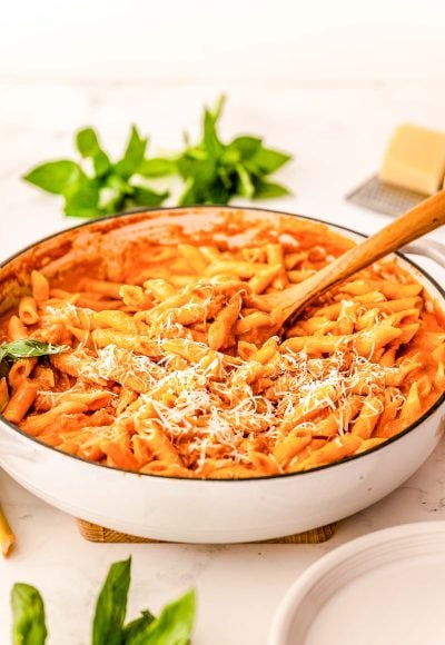 A large skillet filled with penne in vodka sauce with a wooden serving spoon in it.