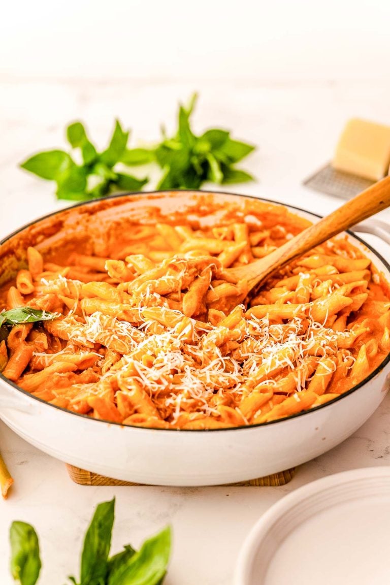 A large skillet filled with penne in vodka sauce with a wooden serving spoon in it.