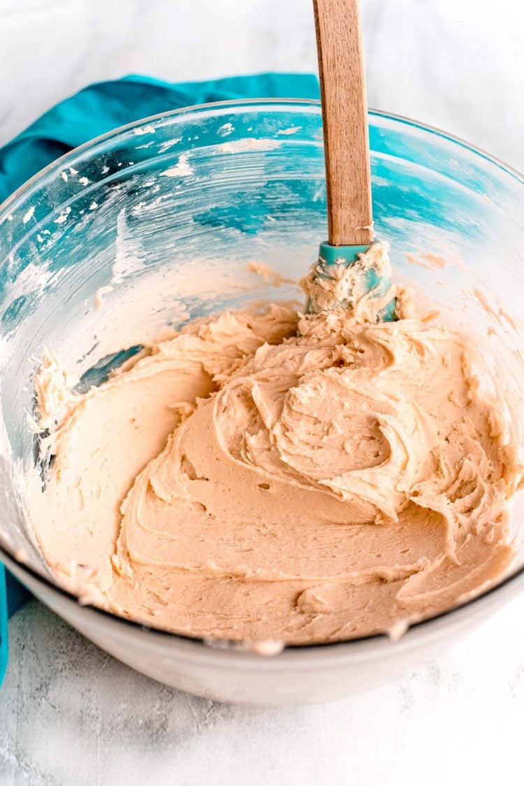 Brown sugar frosting in a glass mixing bowl with a rubber spatula.