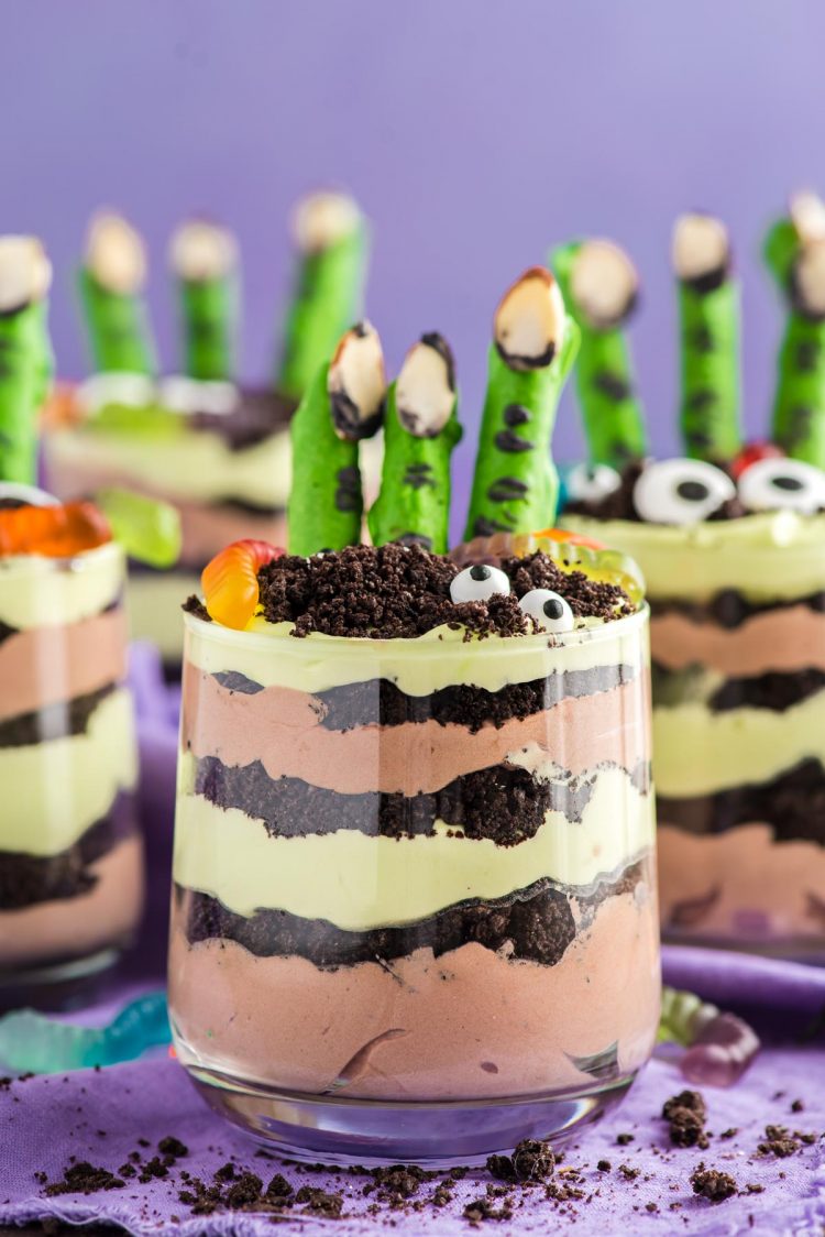 Close up photo of layers Halloween dirt cups with pretzel stick witch fingers, candy eyes, and gummy worms.