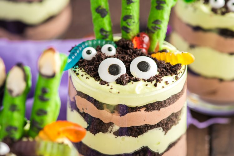 Close up photo of layers Halloween dirt cups with pretzel stick witch fingers, candy eyes, and gummy worms.