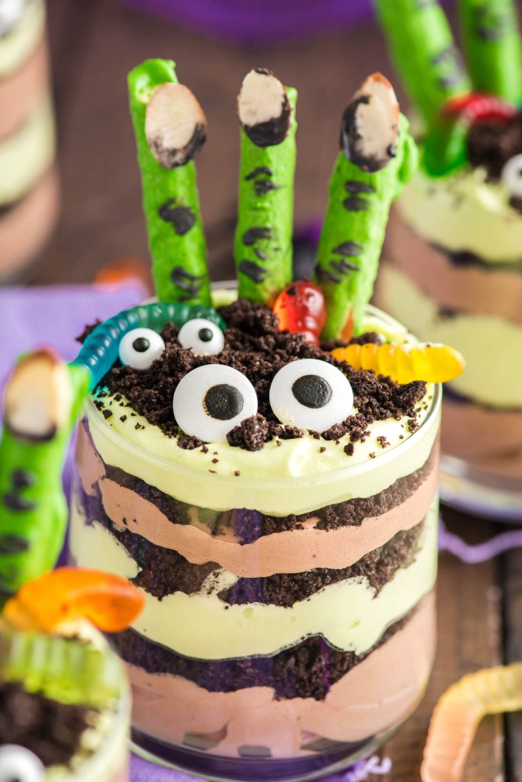 Close up photo of layers Halloween dirt cups with pretzel stick witch fingers, candy eyes, and gummy worms.