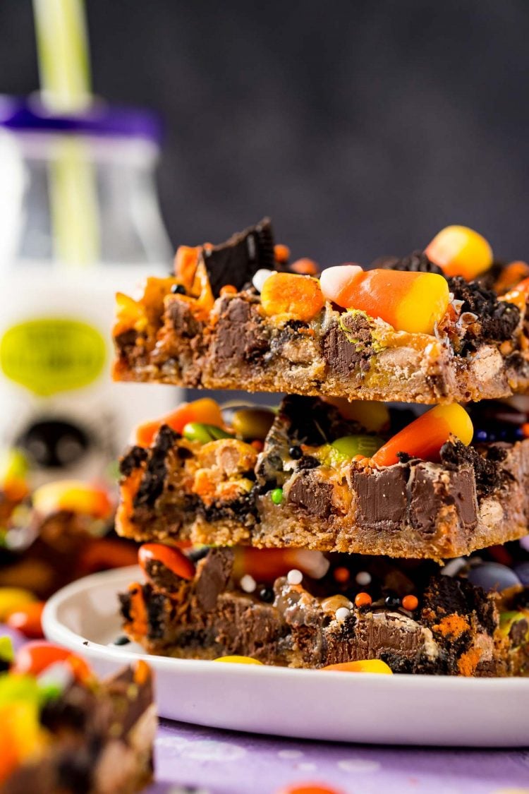 Close up photo of Halloween themed cookie bars on a white plate, stacked three high with a bottle of milk in the background.