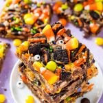 A stack of three halloween magic cookie bars on a small white plate on a purple surface.