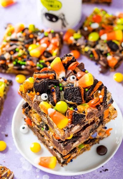 A stack of three halloween magic cookie bars on a small white plate on a purple surface.