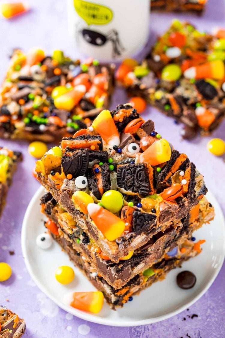 A stack of three halloween magic cookie bars on a small white plate on a purple surface.