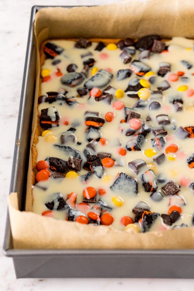 Sweetened condensed milk drizzled over the top of cookies bars topped with candy.