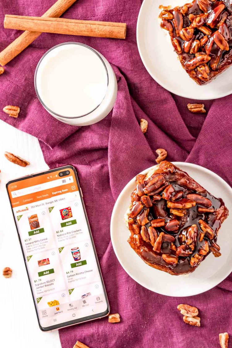 Overhead photo of sticky buns on small white plates with a phone next to them open to the Shaw's app.