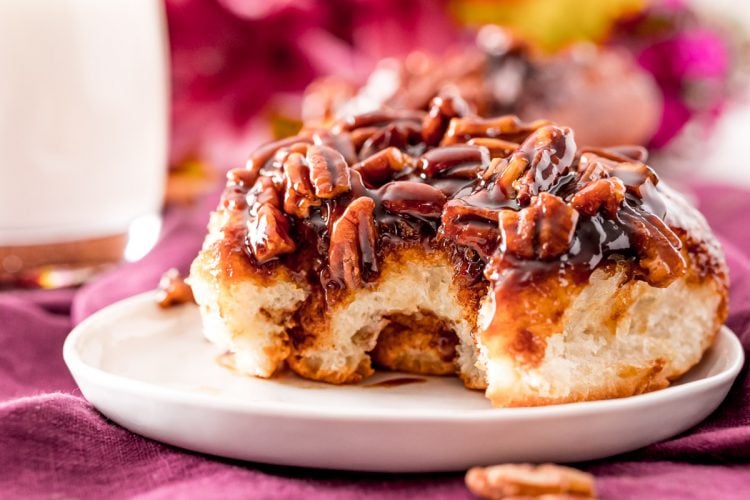 Close up photo of a sticky cinnamon roll on a small white plate with a bite taken out of it.