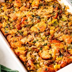 Close up photo of sausage stuffing in a white baking dish with a green napkin next to it.