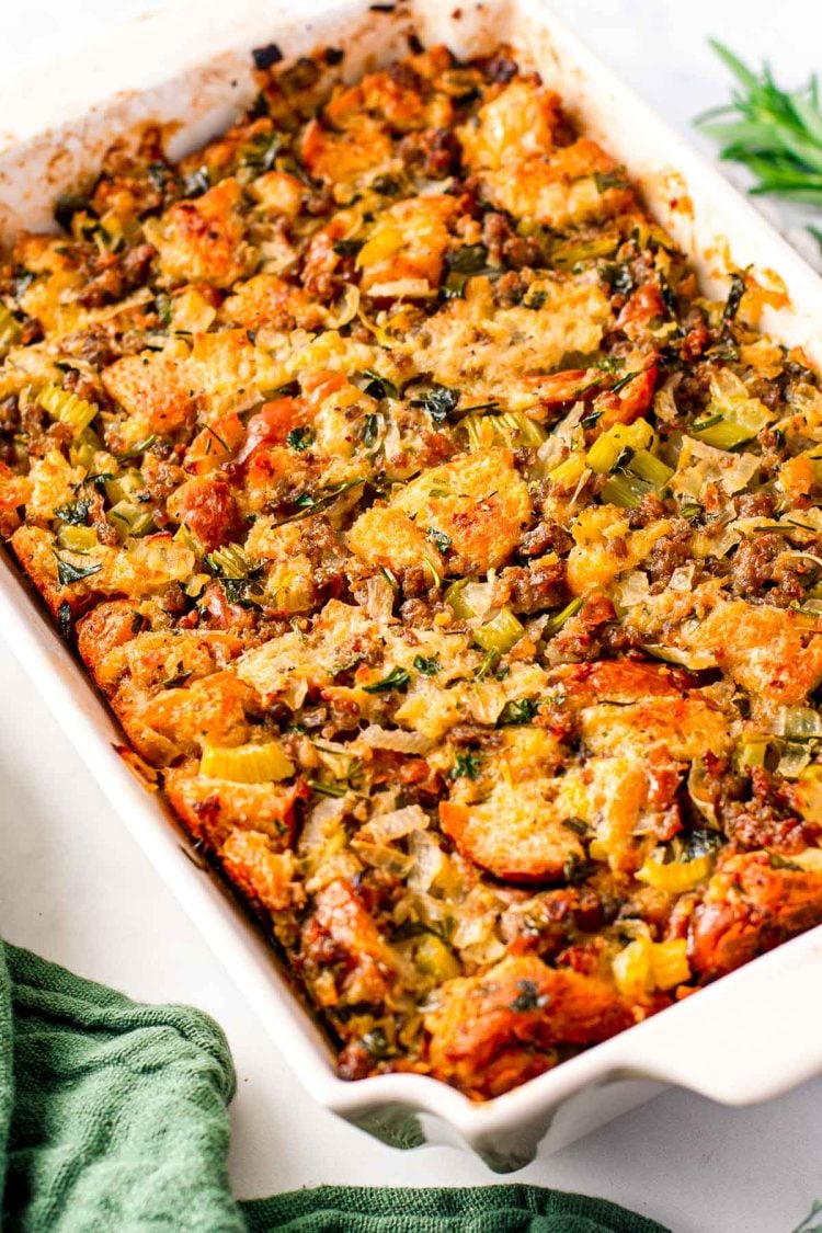 Close up photo of sausage stuffing in a white baking dish with a green napkin next to it.