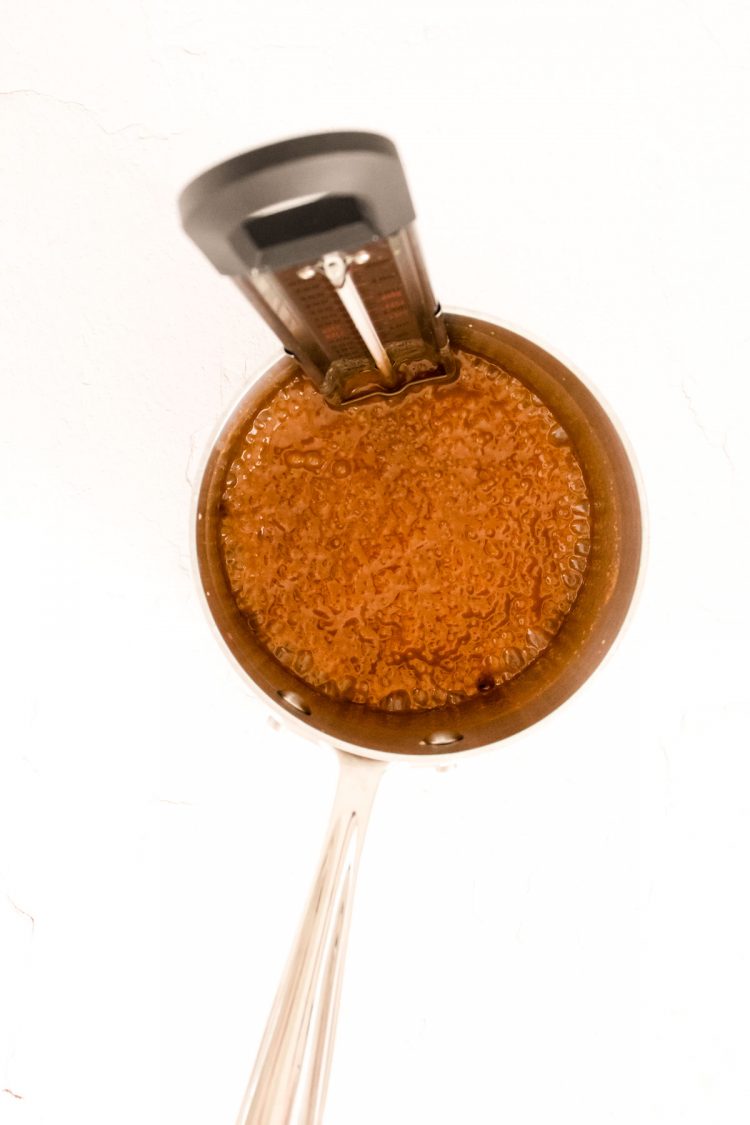 Caramel being made in a small saucepan with a candy thermometer in it.