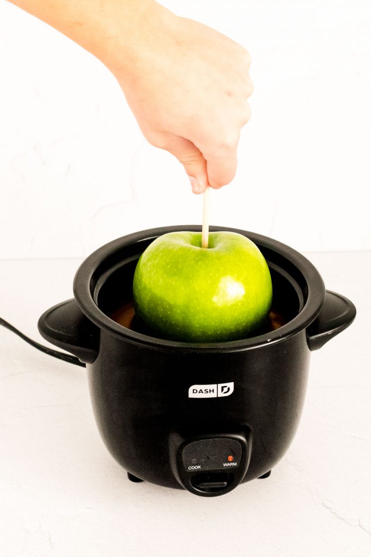 A green apple being dipped in a small crockpot filled with caramel.
