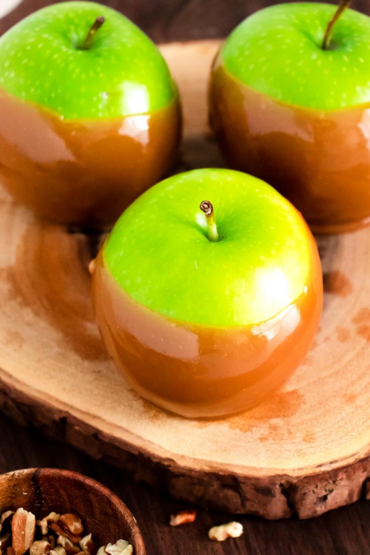 Close up photo of caramel apples on a wooden cake stand.