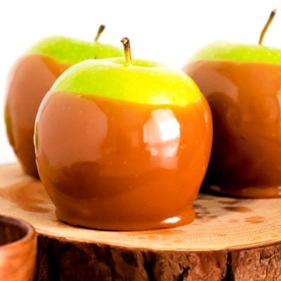 Close up photo of a candied apple on a wooden serving tray.