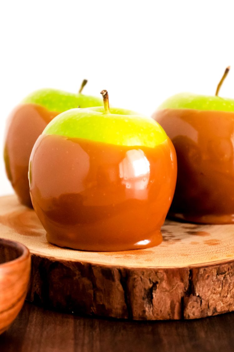 Close up photo of a caramel apple on a wooden serving tray.