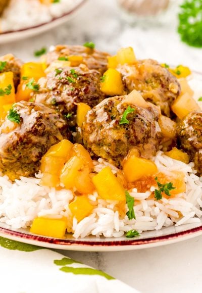 Close up photo of sweet and sour meatballs on a bed of white rice with pineapple.
