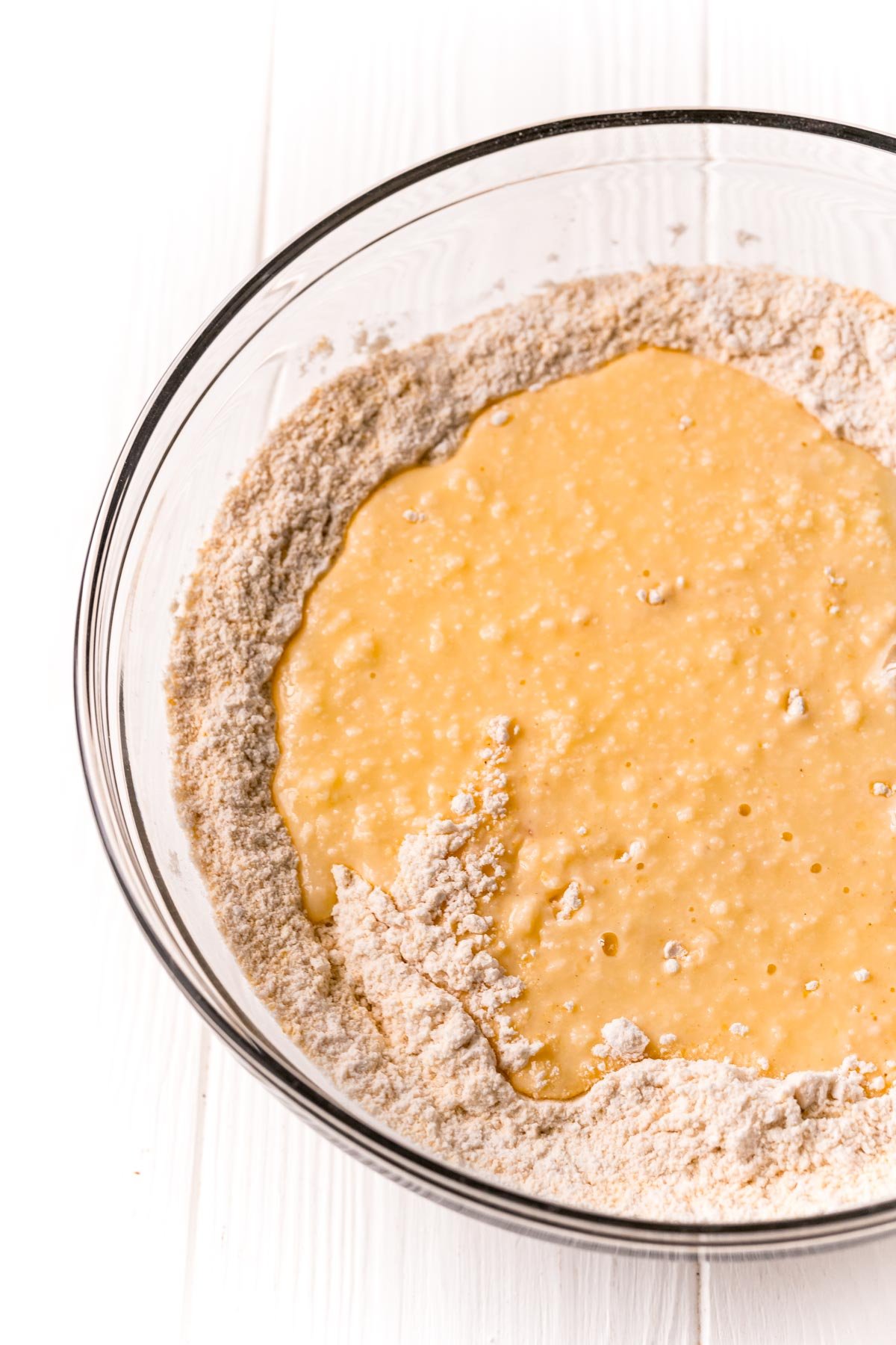 Wet ingredients being poured into a mixing bowl of dry ingredients to make cornbread.