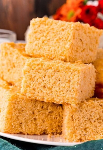 Close up photo of corn bread slices stacked on top of each other on a white plate.