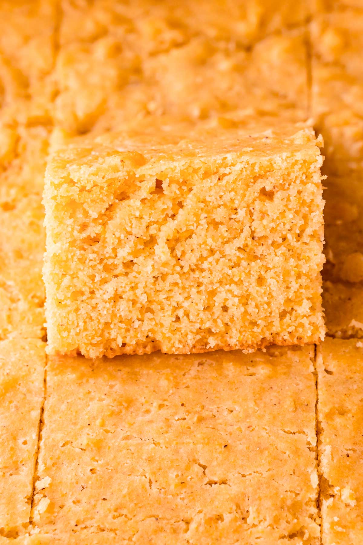 Close up photo of a pan of cornbread where one slice is tipped up out of the pan. 